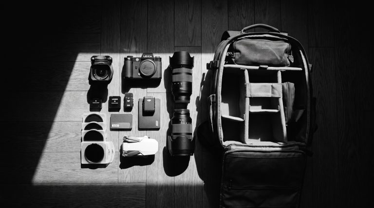 Camera gear flat lay with mirrorless camera, lenses, drone and accessories next to a travel backpack